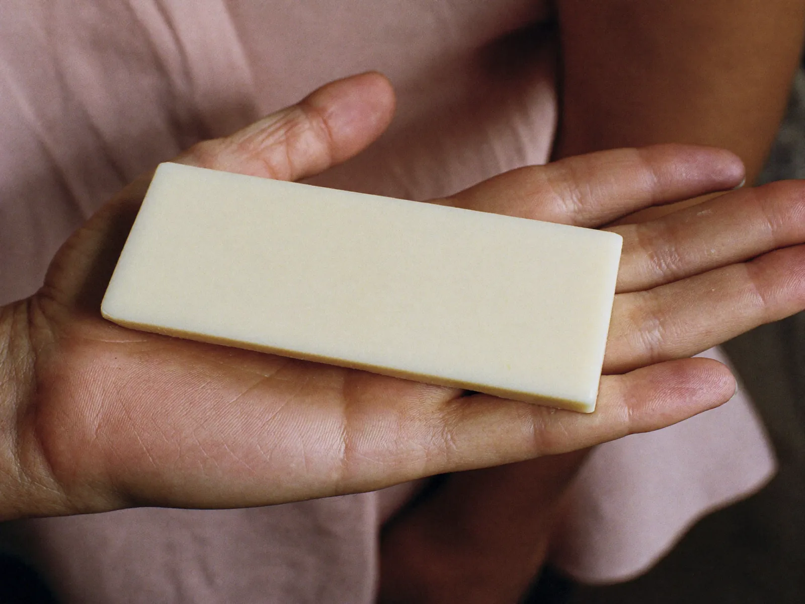 A large pale cream rectangular bar of soap resting in an adult’s open palm.